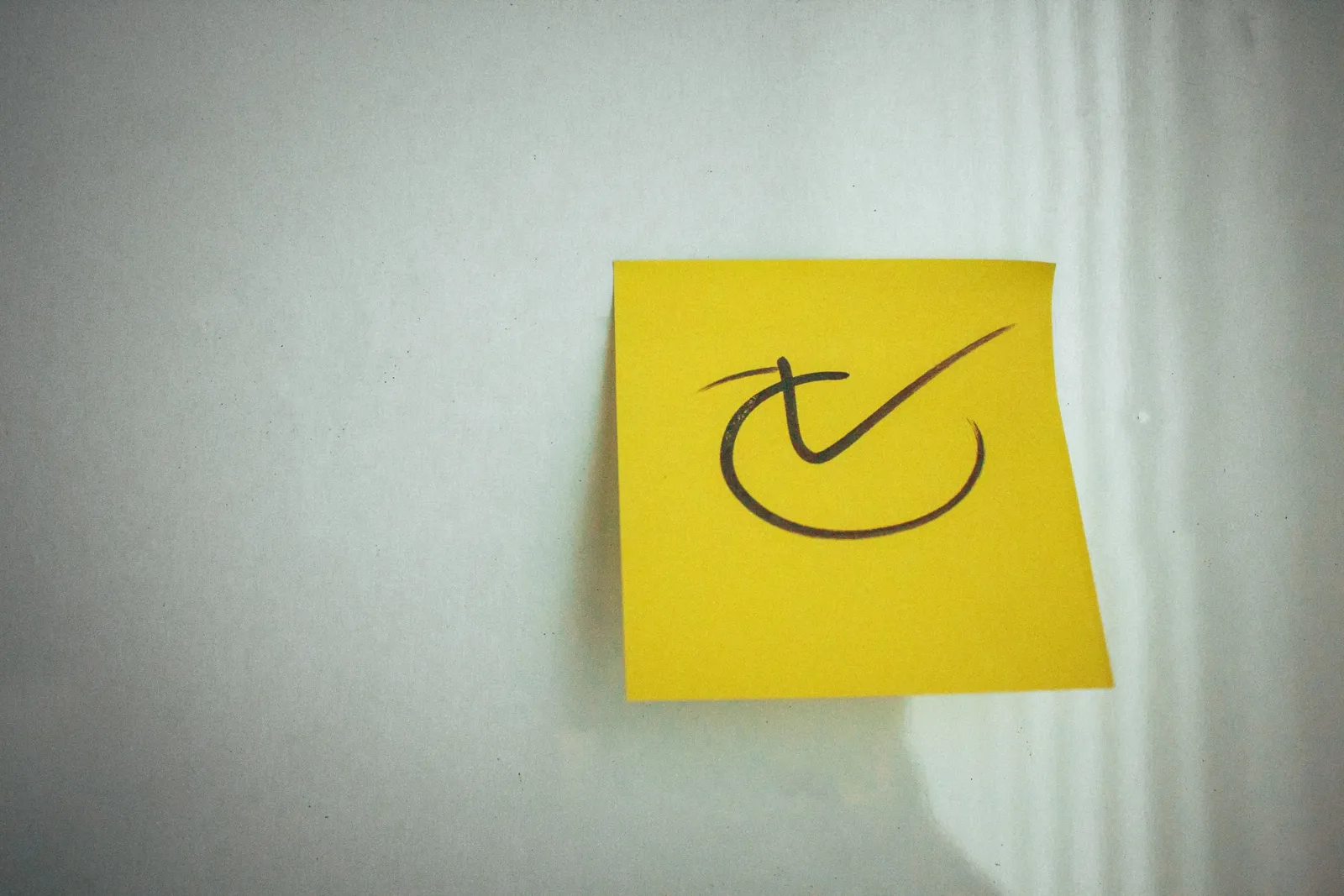 Yellow sticky note with a hand-drawn tick on a light wall