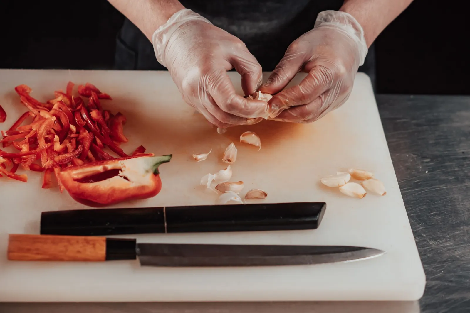 Hands in disposable gloves preparing food on a chopping board